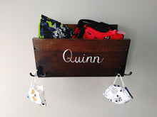Load image into Gallery viewer, Are you looking for storage for your kid's items? Each wooden storage bin is the perfect option for your entryway to keep coats, masks, hats and small toys and books all in one place. The storage bin has two hooks on the front for additional hanging storage and is finished in your choice of stain colour. It can be personalized with a name in calligraphy font in your choice of colour. All items are handmade with care and are one of a kind.