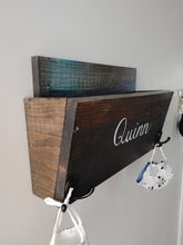 Load image into Gallery viewer, Are you looking for storage for your kid's items? Each wooden storage bin is the perfect option for your entryway to keep coats, masks, hats and small toys and books all in one place. The storage bin has two hooks on the front for additional hanging storage and is finished in your choice of stain colour. It can be personalized with a name in calligraphy font in your choice of colour. All items are handmade with care and are one of a kind.