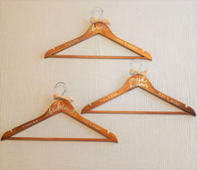 Load image into Gallery viewer, Wood hangers are hand-lettered with the bride's, maid of honour and bridesmaid name and the wedding date. All titles are written in calligraphy on the centre of the hanger, and their name and the wedding date in block lettering with your choice of gold or chrome font colour.