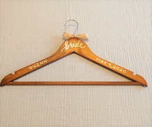 Load image into Gallery viewer, Wood hangers are hand-lettered with the bride's name and your wedding date. "bride" is written in calligraphy on the centre of the hanger, and the bride's name and your wedding date in block lettering with chrome font colour.