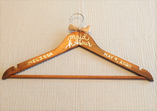 Load image into Gallery viewer, If you are looking for a perfect gift for your maid of honour here is a custom hanger to accent her beautiful dress. Wood hangers are hand-lettered with the maid of honour’s name and the wedding date. "maid of honour” is written in calligraphy on the centre of the hanger, and the maid of honour’s name and your wedding date in block lettering with your choice of gold or chrome font colour.