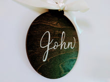 Load image into Gallery viewer, Each holiday wood ornaments is stained your choice of colour, and can be personalized with a name or small phrase in your choice of font colour.  Each ornament has a ribbon tied in a bow that is included.  Baltic Birch 4 inch round, 3mm thick.
