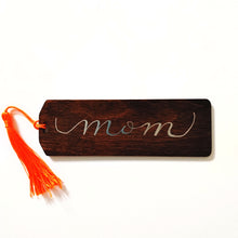Load image into Gallery viewer, Do you have a book lover in your life?   Each bookmark is stained your choice of colour, and can be personalized in your choice of font colour. Each bookmark has a colourful tassel included.   Baltic Birch 2x6 inches, 3mm thick This espresso stained bookmark in a rectangular shape has a beveled edge. &quot;mom&quot; is written in calligraphy and silver font. 
