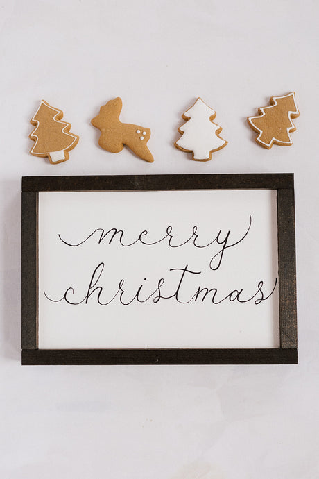 This Merry Christmas framed wood sign is handwritten in flowy calligraphy font with an espresso colored frame. This handmade sign is surrounded by homemade gingerbread cookies 
