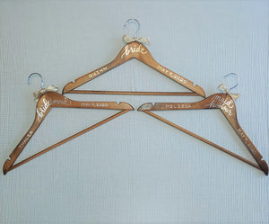 Wood hangers for the bride, maid of honour and bridesmaid are hand-lettered with the name and the wedding date. Wedding title is written in calligraphy on the centre of the hanger, and the name and the wedding date in block lettering with your choice of gold or chrome font colour.