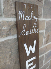 Load image into Gallery viewer, A personalized welcome sign can be a warm, welcoming piece at the entrance of your home with a family name that can be added to the top of the sign.  Each sign is vertically hand lettered with “WELCOME” that is painted white down the center of the sign on a 48x7 inch solid wood sign. Each sign is stained in your choice of colour and sealed for weather resistance. Are you looking for custom font colour please let me know!   Please allow me up to two weeks to produce your Welcome sign.  
